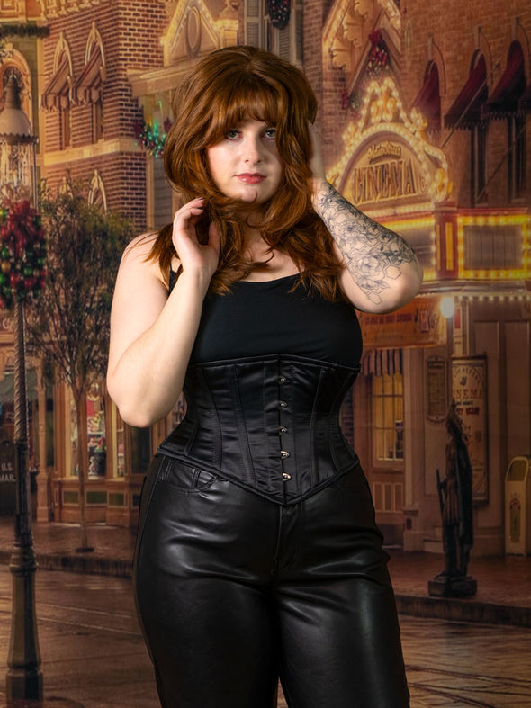 cute corset model wearing the cs201 black satin waist  training corset with black leather pants and her hands in her hair