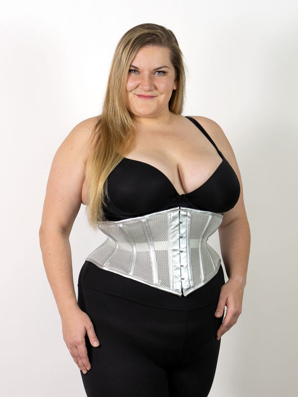 plus size model wearing a silver mesh corset with faux metallic leather trim over black leggings and black bra