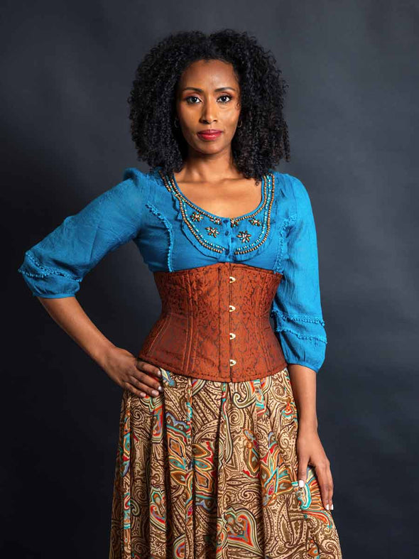 Model wearing a turquoise beaded shirt and multi colored skirt and a cinnamon brown brocade waist training corset