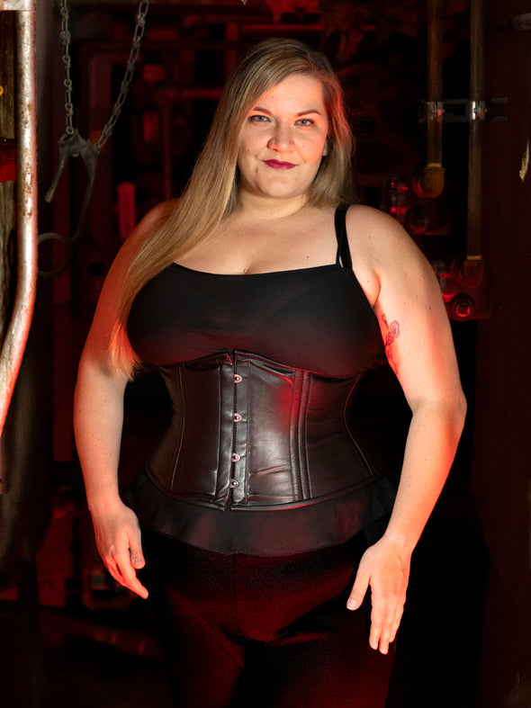 halloween corset image with model wearing black pants and a black sheer top under her black leather plus size corset 