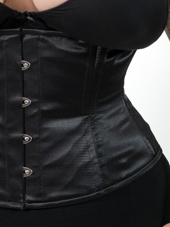 close up detail view of a plus size corset model wearing a cs411 standard romantic curve waist training black corset with a black bra and black leggings