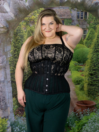 cute curvy Model in an english garden wearing a plus size black mesh corset with a lace corset top and dark pants