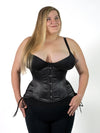 cute curvy plus size corset model wearing a black satin corset with hip ties over a black bra and leggings