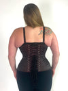 cute curvy plus size corset model wearing a shimmering maroon corset over a black bra and leggings back lace up corset view