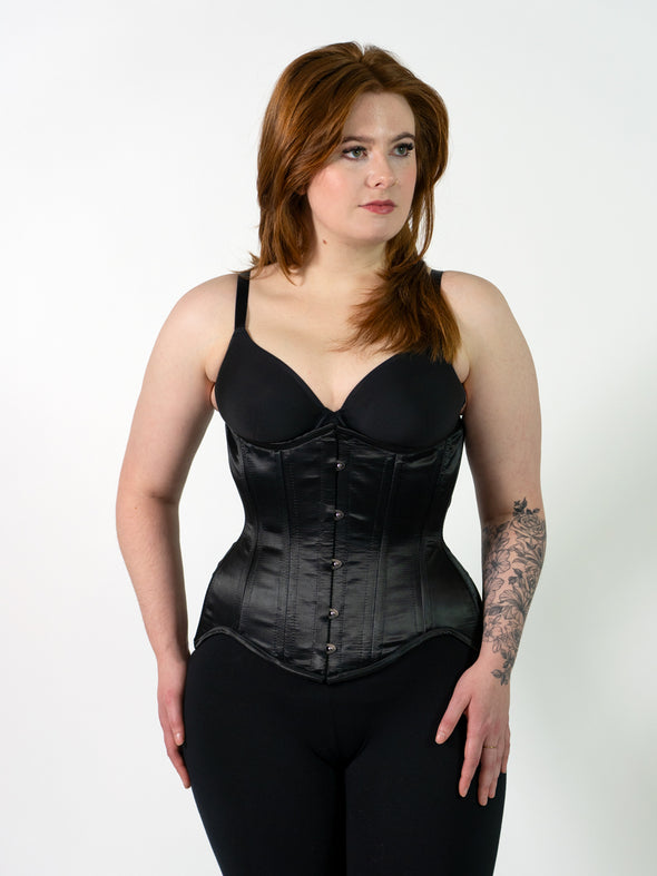 cute model wearing the cs479 longline extreme curve black satin waist training corset with leggings and a black bra