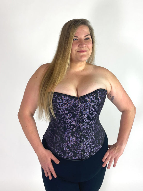plus size model wearing a purple brocade  overbust steel boned corset top with black leggings