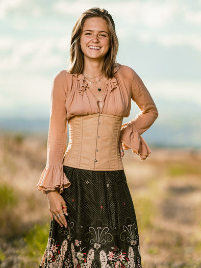 cute corset model wearing a beige cotton corset over a nude colored ruffled blouse with a black floral skirt